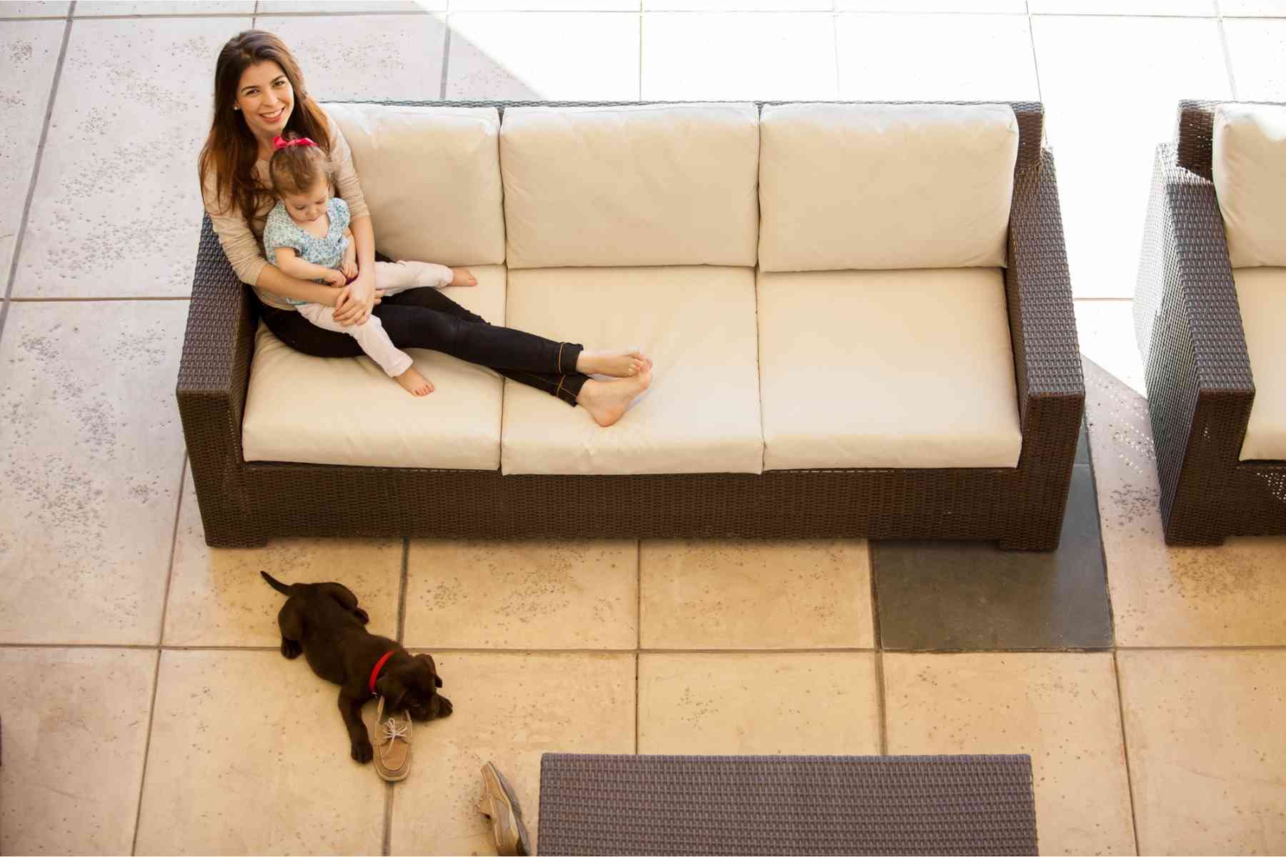 Black puppy sleeping on a shoe while mother and baby daughter are sitting on a sofa